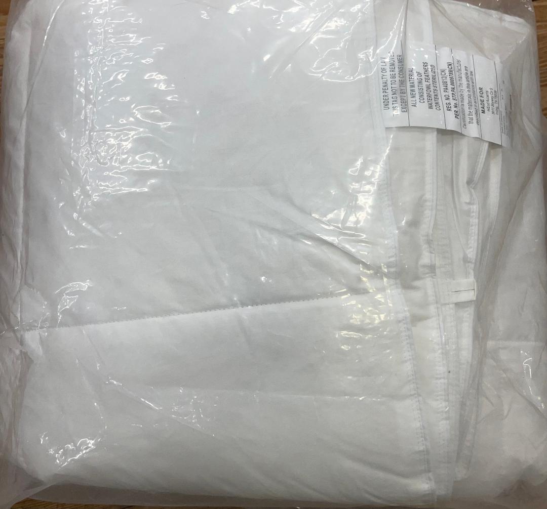 A rolled-up white mattress pad wrapped in plastic, with a label visible on the top side.