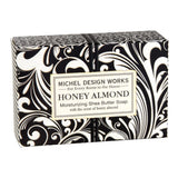 A bar of soap with a black and white floral patterned wrapper, labeled 'Michel Design Works Honey Almond Shea Butter Soap'.