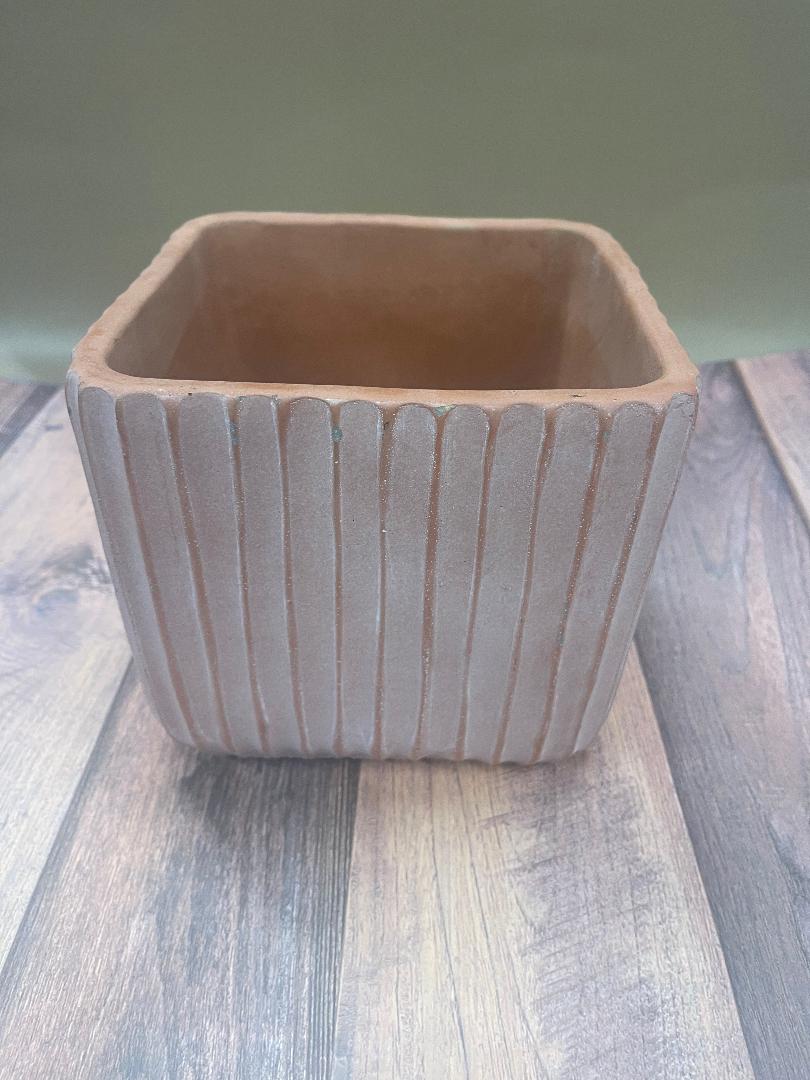 A beige or orange ridged planter with a sturdy base, placed on a wooden surface.