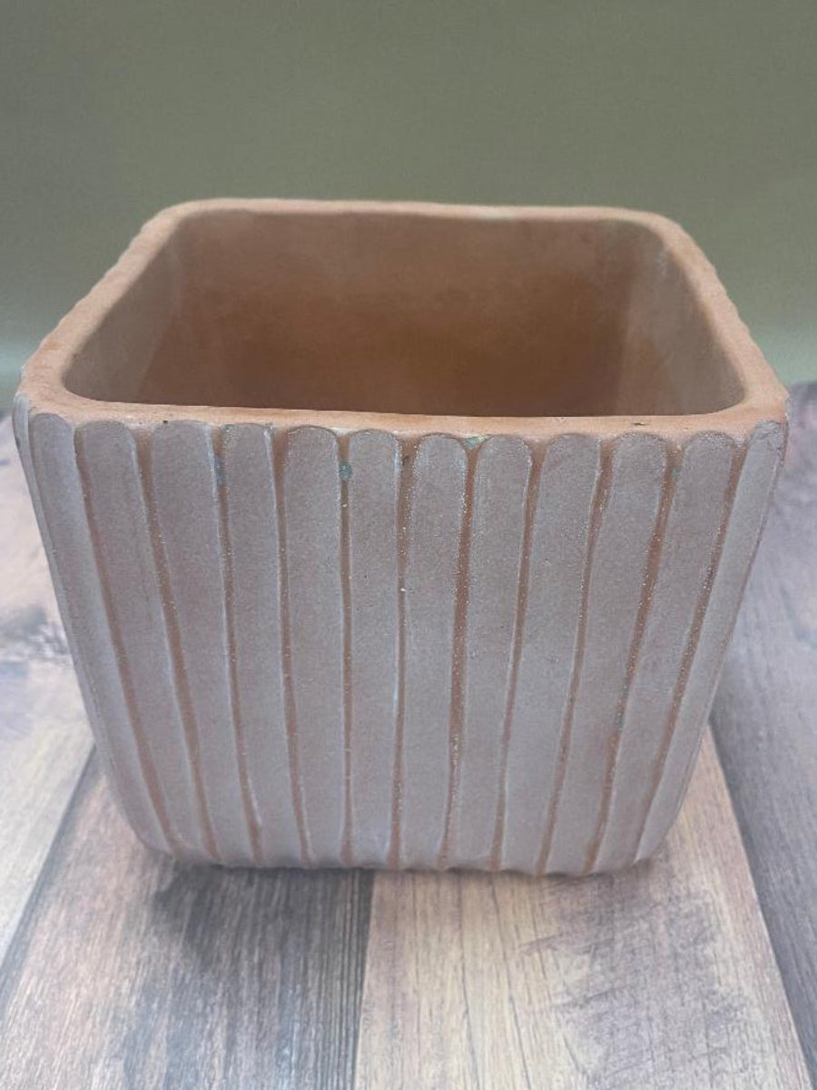 A beige or orange ridged planter with a sturdy base, placed on a wooden surface.