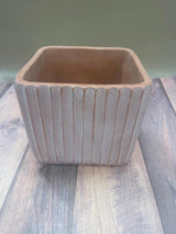 A beige or orange ridged planter with a sturdy base, placed on a wooden surface.