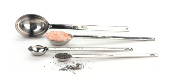 A set of stainless steel measuring spoons and a scoop, with the spoons laying in a row and the scoop in front of them, all containing small measures of a substance.