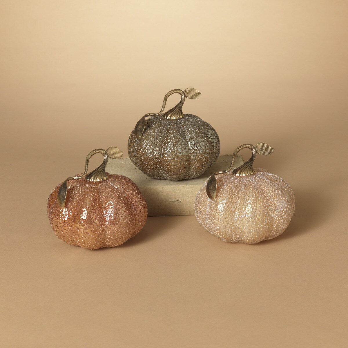 Three handblown glass pumpkins of varying sizes, with a translucent finish in shades of orange, pink, and clear, displayed against a neutral background.