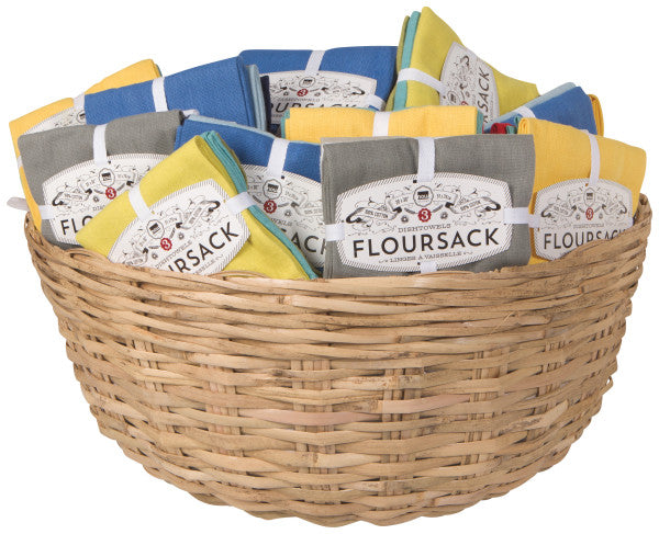 A set of three folded blue flour sack dish towels placed in a brown wicker basket.
