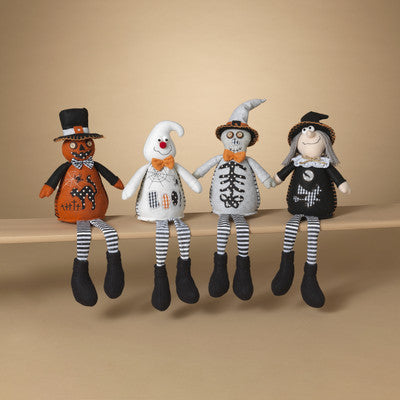 A set of plush Halloween figures including characters that resemble a pumpkin, a ghost, a skeleton, and a witch, arranged in a line on a shelf.