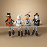 A set of plush Halloween figures including characters that resemble a pumpkin, a ghost, a skeleton, and a witch, arranged in a line on a shelf.