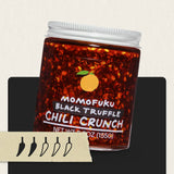 Jar of Momofuku Black Truffle Chili Crunch with a label and chili pepper icons on a light background