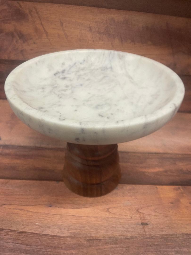 A white marble pedestal bowl with a brown base made of acaia wood, placed on a wooden surface.