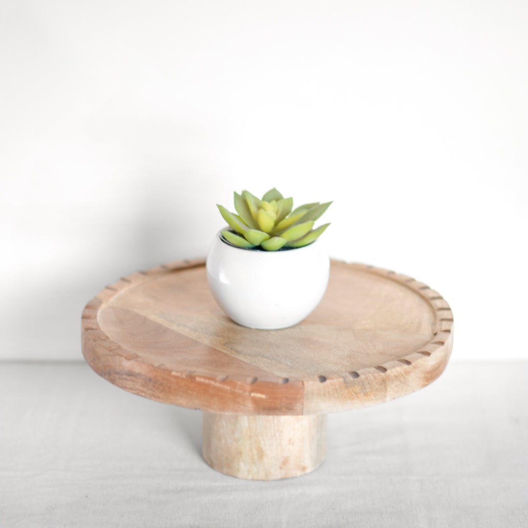 A round, burnt wood cake stand with a white cake plate on top, set against a neutral background.