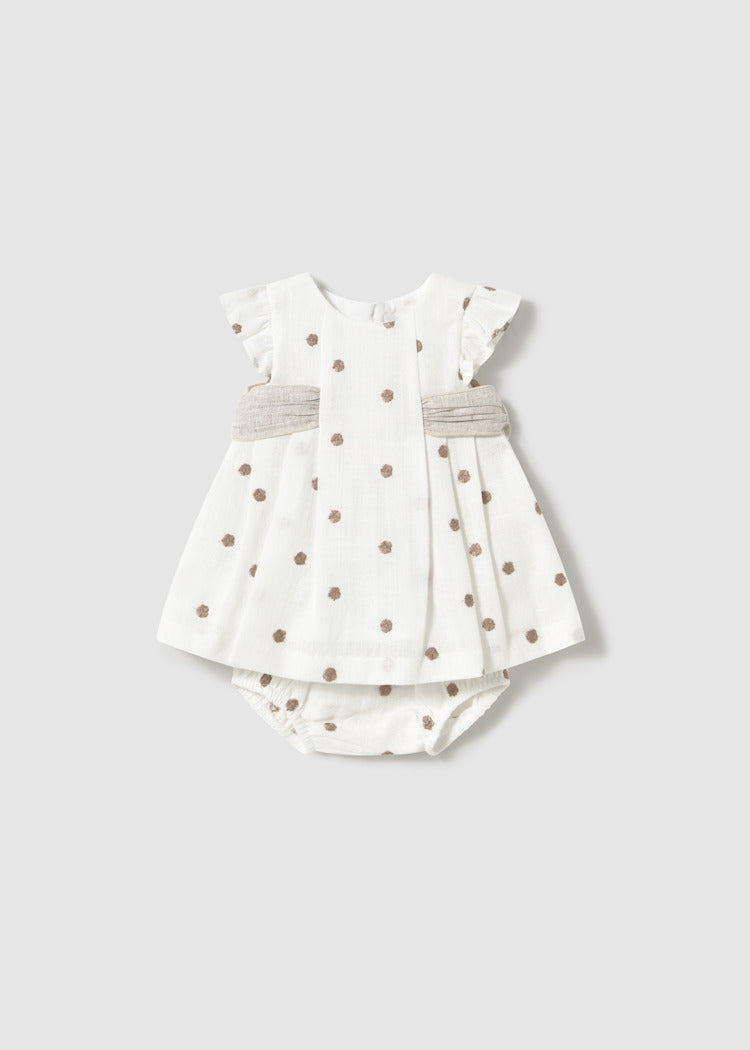 White baby dress with brown polka dots and matching bloomers on a plain background