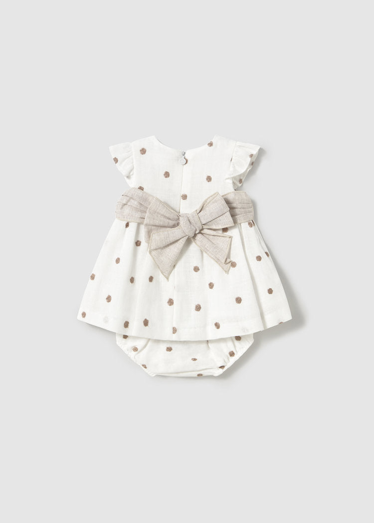 Baby outfit with polka dot dress and bow on a plain background