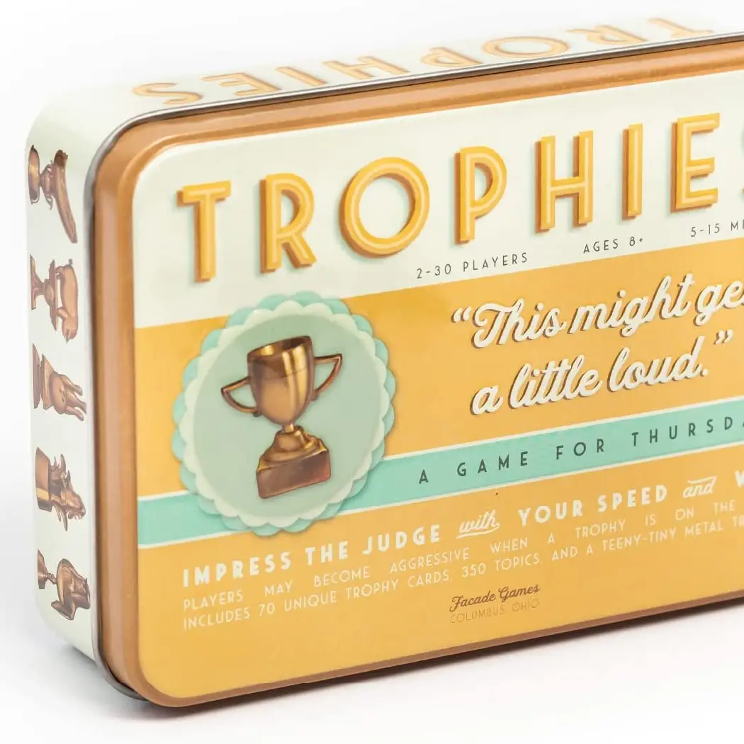 The image shows a product packaging for 'TROPHIES PARTY CARD GAME'. It features a vintage style design with trophy illustrations and text detailing the game's features, such as being suitable for 2-30 players, ages 8 and up, and including 70 unique trophy cards and 350 topics.