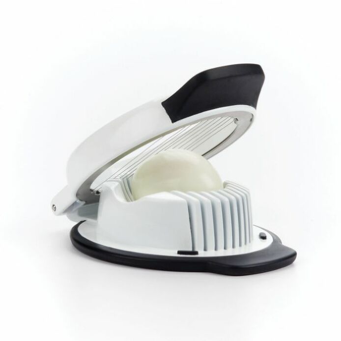 An OXO Good Grips Egg Slicer in white color with a black top lever, shown with an egg being sliced, placed against a white background.