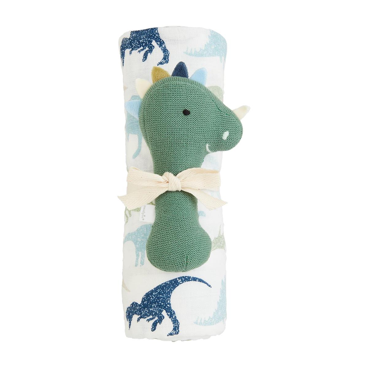 A swaddling blanket with a dinosaur rattle attached to it. The blanket has a pattern with dinosaurs and the rattle is also dotted with dinosaurs.