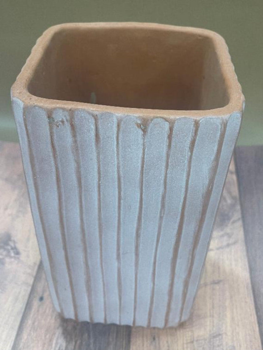 A beige ceramic tall planter with horizontal ridges, displayed on a wooden surface.