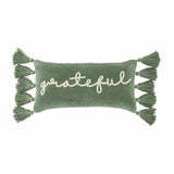 A rectangular green velvet pillow with the word 'grateful' written in a white script font, adorned with green tassels on the sides.