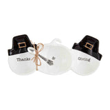 Two white ceramic dishes with black Pilgrim hats on top, one labeled 'Thanks' and the other ' Giving', tied with a decorative ribbon, and a small ceramic turkey.