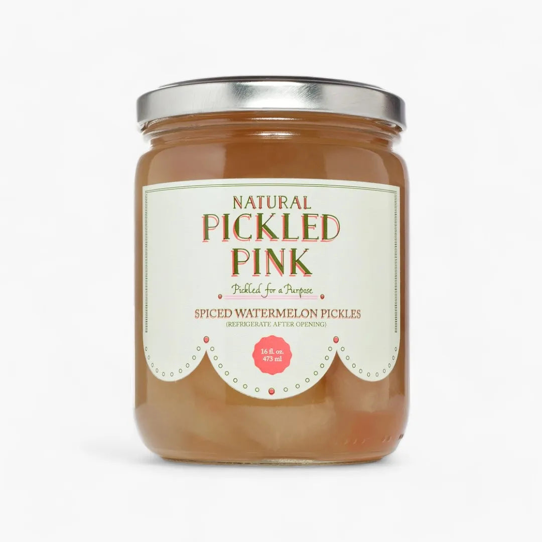 A glass jar of Natural Pickled Pink Spiced Watermelon Pickles with a silver metal lid and a cream-colored label, set against a plain white background.