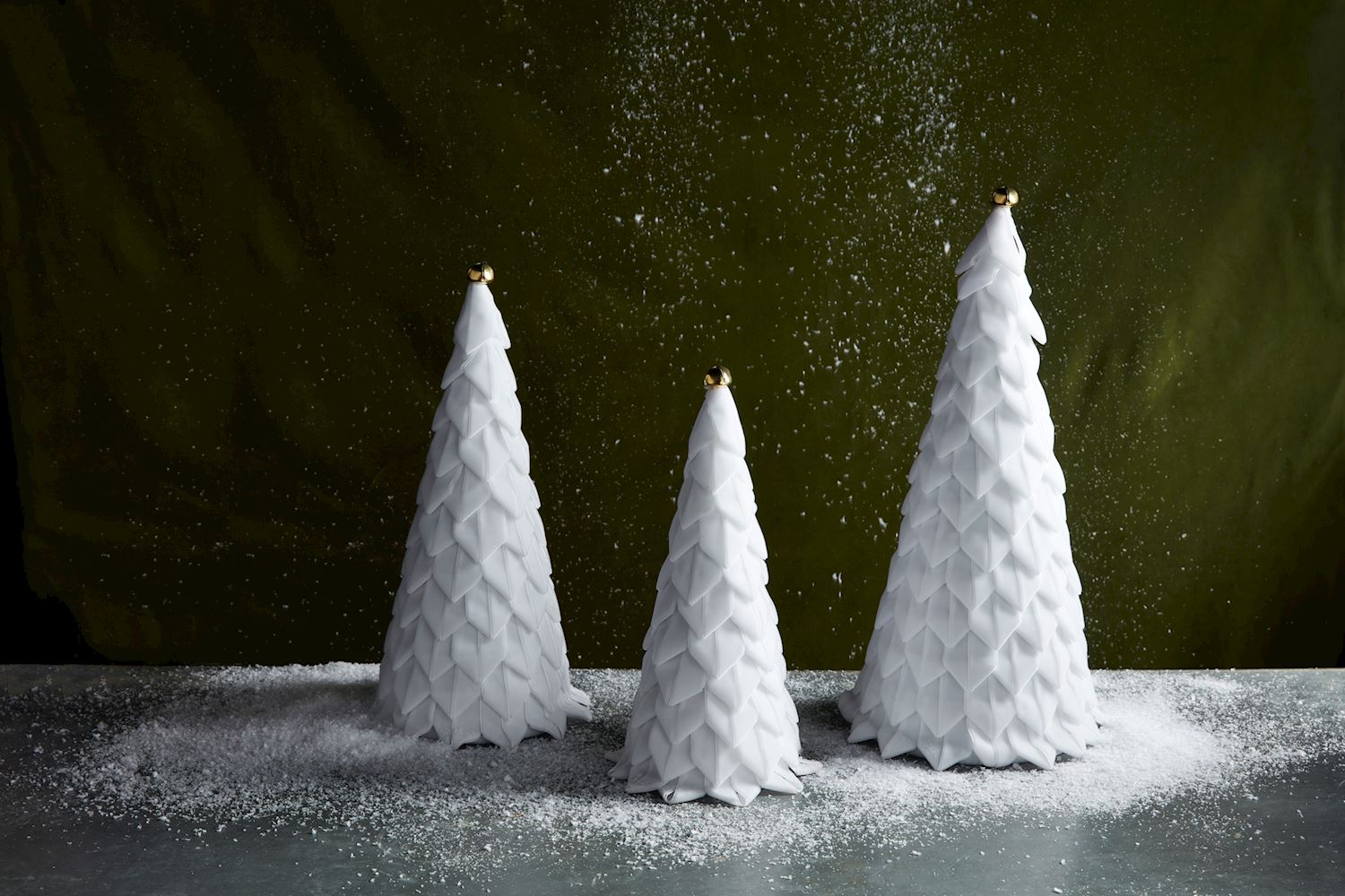 Three white velvet tree toppers of different sizes, designed with a textured, geometric pattern, displayed against a dark background with snow-like particles in the air.