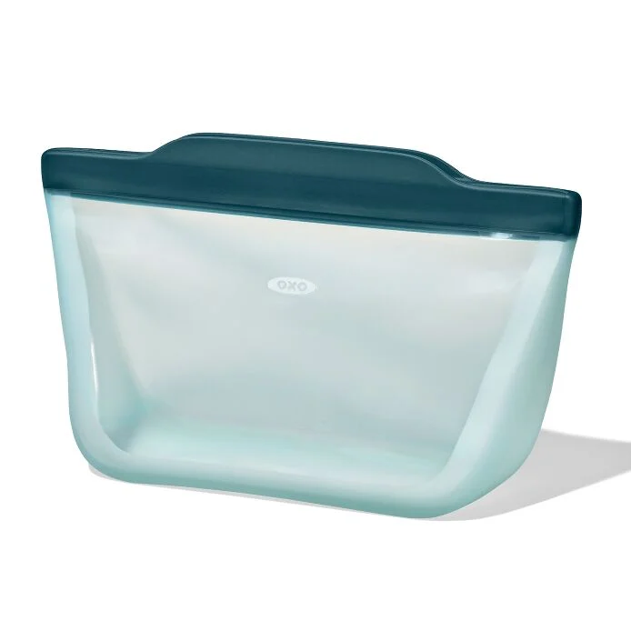 A clear silicone food storage bag with a blue lid and a snap closure.