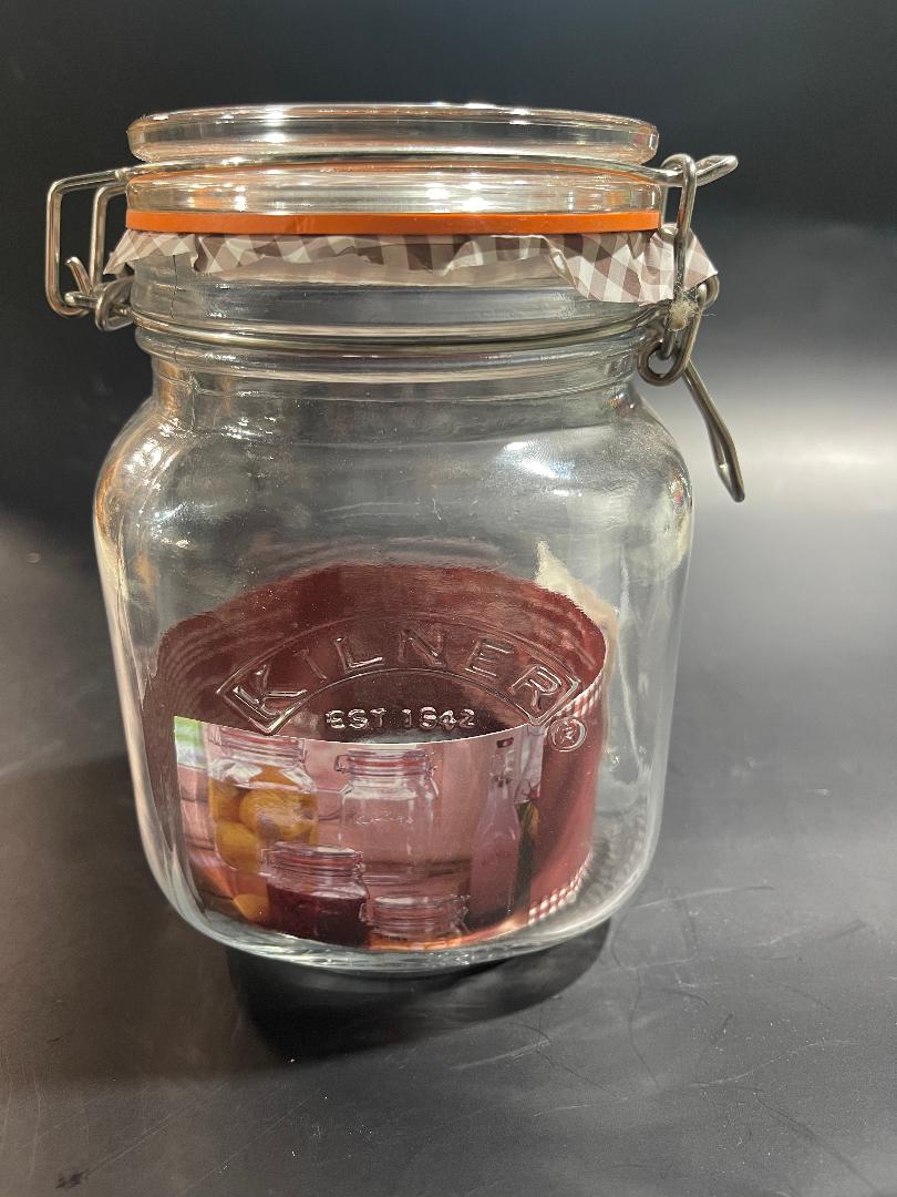 A clear glass clip top square jar with a red and black lid, containing what appears to be coffee or tea bags.