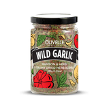 A clear plastic jar containing dried herbs with a label that reads 'Wild Garlic' and the brand name 'Olivelle'. The jar is sealed with a black lid and the product is depicted with a colorful graphic of garlic and tomato, indicating the flavor profile.