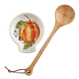 A white spoon rest with a painted pumpkin design and a wooden spoon next to it.