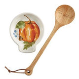 A white spoon rest with a painted pumpkin design and a wooden spoon next to it.