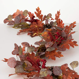 A decorative garland with artificial leaves, pinecones, and red berries against a white background.