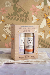 A gift set containing two jars of balm, one labeled for heel care and the other for body balm, packaged in a cardboard box with a floral design.