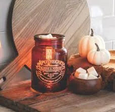 Jar candle with a decorative label on a wooden surface with pumpkins and marshmallows.