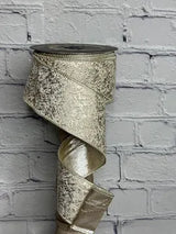 A roll of metallic gold glitter ribbon with a textured, shimmering finish, shown unrolled against a white painted brick wall background.
