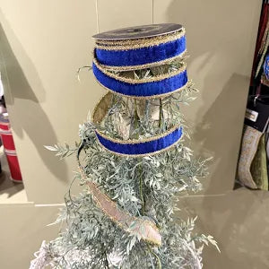 A decorative flocked Christmas tree with silver-white needles, wrapped with three blue and gold ribbons, in an indoor setting.