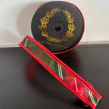 A roll of red ribbon with a gold wreath design and a plaid patterned section, displayed on a dark surface.