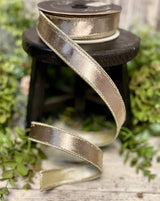 Spool of gold ribbon with a decorative edge on a wooden surface with greenery in the background