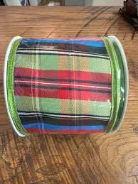 A roll of plaid ribbon with green glitter edges, featuring a multicolor pattern of red, green, blue, and black stripes, displayed on a wooden surface.