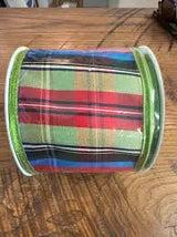 A roll of plaid ribbon with green glitter edges, featuring a multicolor pattern of red, green, blue, and black stripes, displayed on a wooden surface.