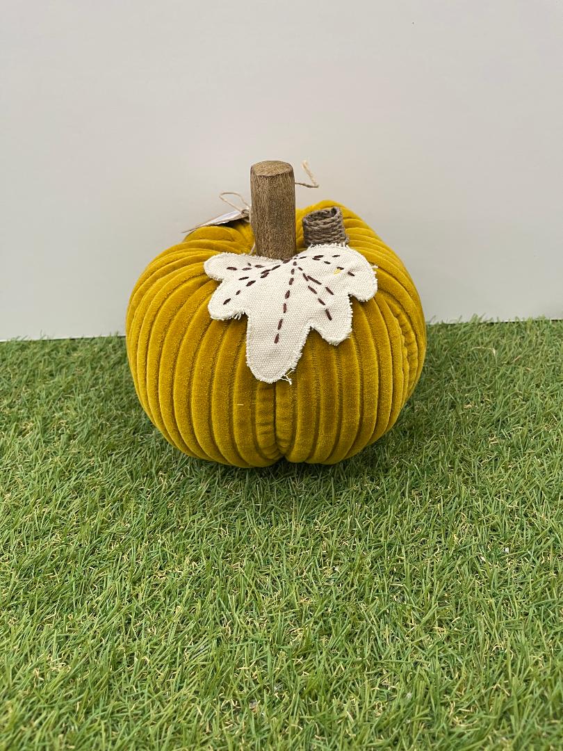 Yellow fabric pumpkin with a white flower on a grassy surface