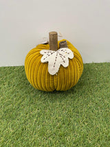 Yellow fabric pumpkin with a white flower on a grassy surface