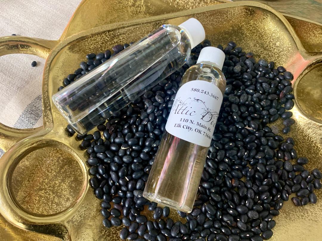 Two bottles of kumquat oil on a gold tray with a pile of black kumquat seeds in front of them.