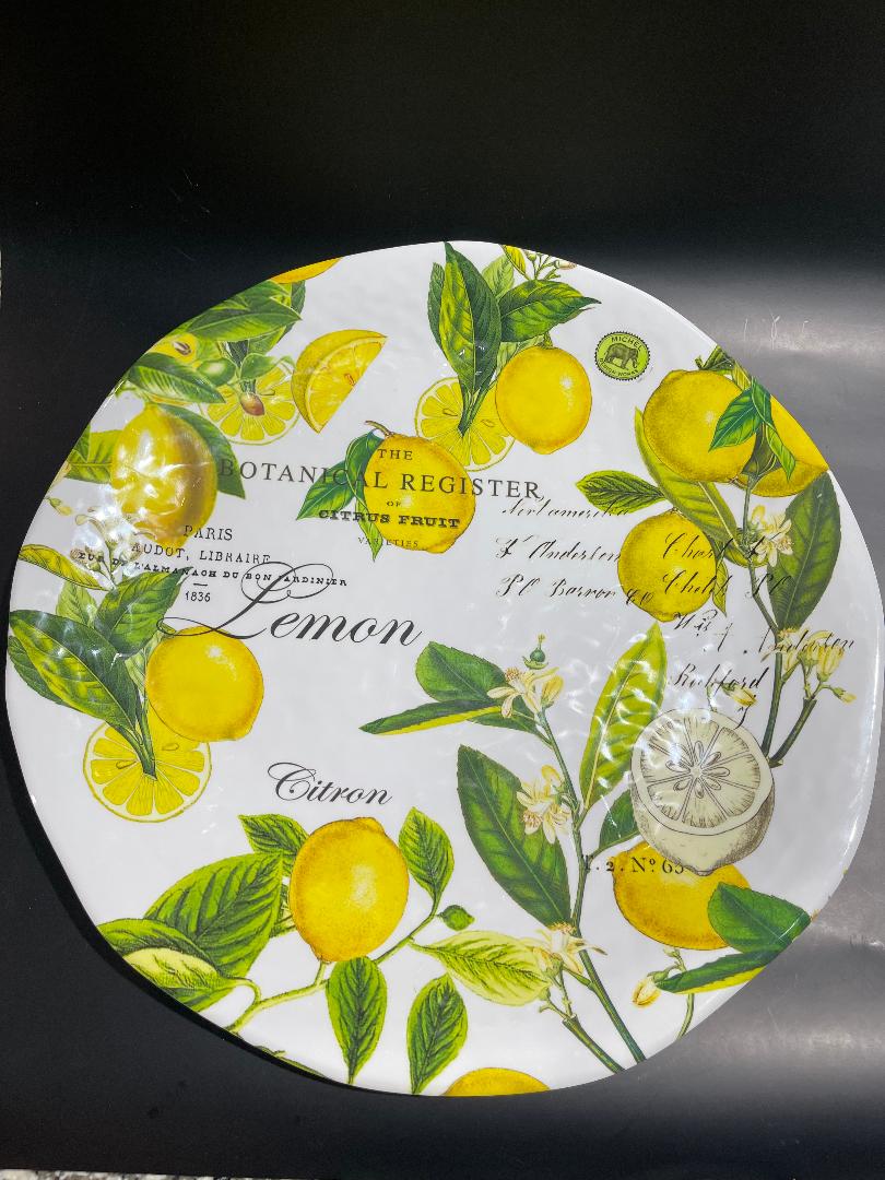 A round decorative platter featuring a vibrant pattern of lemons and basil leaves on a yellow background.
