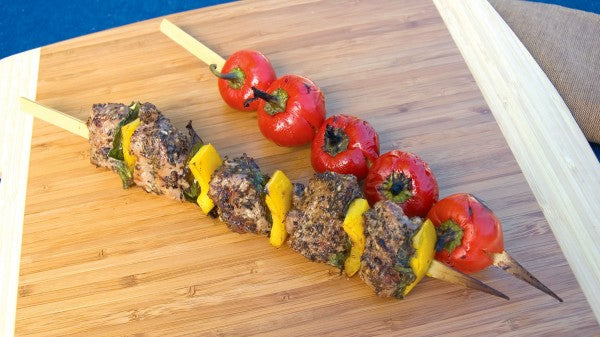 A set of bamboo skewers with food being cooked on them, placed on a wooden board.