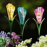 A set of three fiber optic rain gauge garden stakes in a garden, with each stake glowing in different colors.