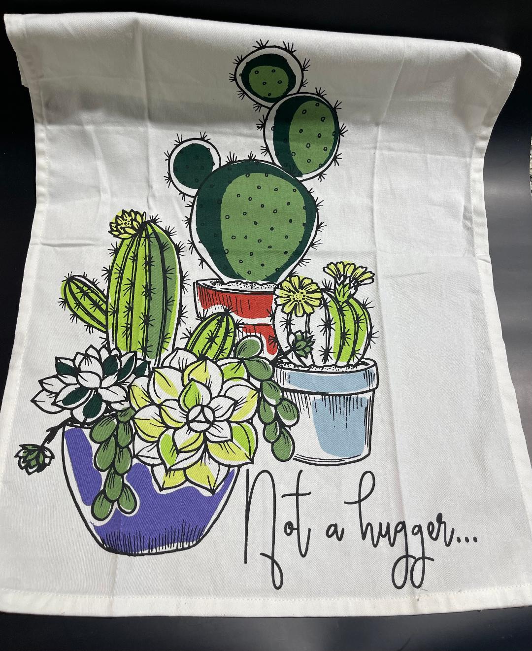 A white kitchen towel with a colorful illustration of various cacti in pots and the phrase 'Not a hugger...' written on it.