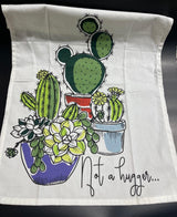 A white kitchen towel with a colorful illustration of various cacti in pots and the phrase 'Not a hugger...' written on it.