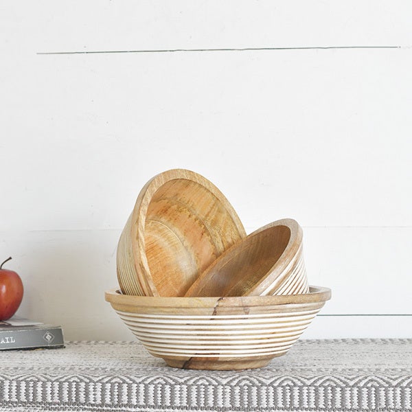 A stack of wooden bowls with a line pattern, placed on a table with a white and gray patterned tablecloth.