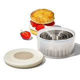 A set of OXO double-sided cookie and biscuit cutters in various sizes, with a flat side and a scalloped side, displayed next to a strawberry shortcake with a biscuit cutter in the background.