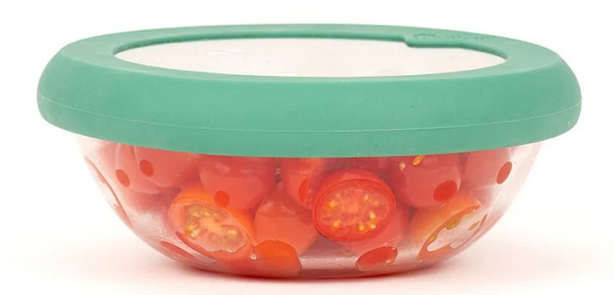A clear plastic food storage container with a green lid, filled with sliced cherry tomatoes.