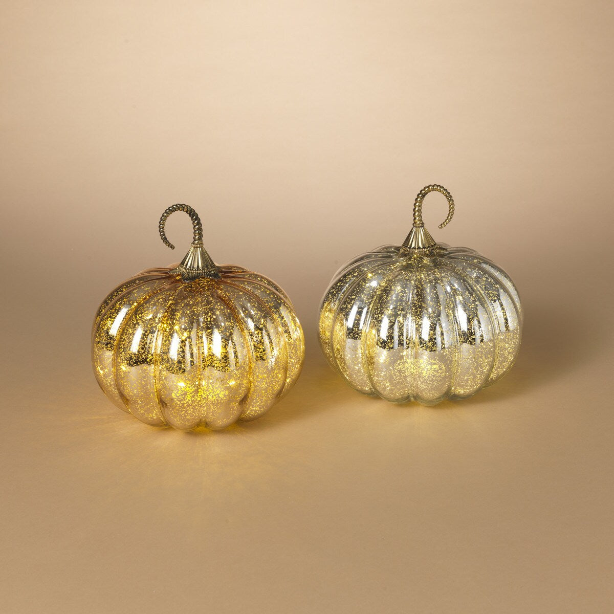 Two pumpkin-shaped lighted mercury glass decorations, one with a gold finish and the other with a silver finish, set against a neutral background.