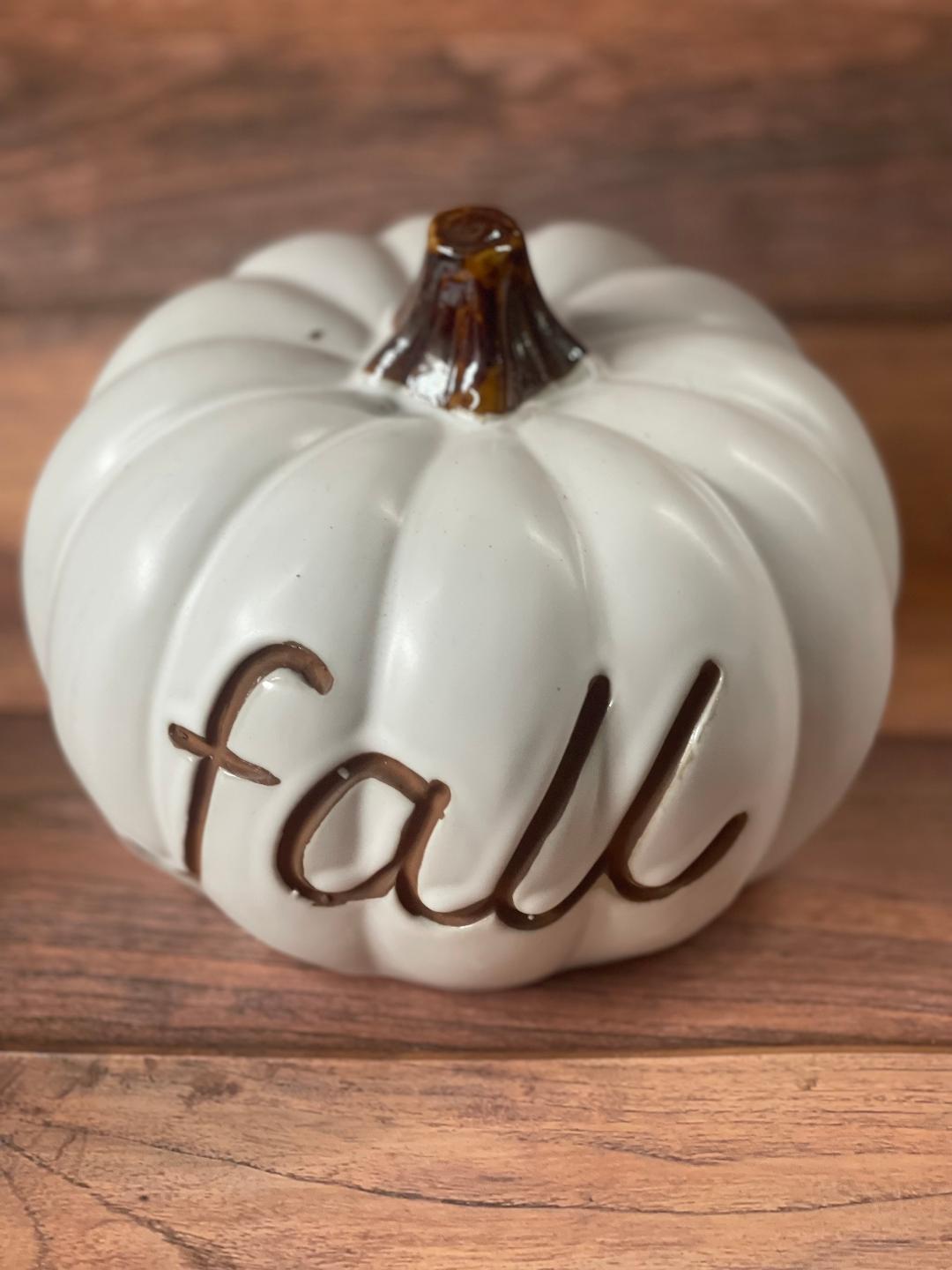 An ivory colored pumpkin resin ornament with the word 'fall' written in brown script on it.